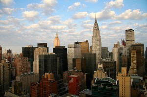 Manhattan skyline centered around the Chrysler building, with blue sky and scattered clouds.