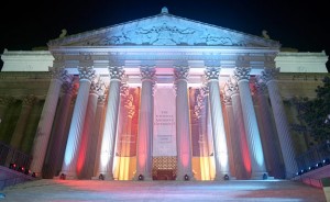 Ornately decorated building with columns. Red, white, and blue colored spot lights are aimed up the columns making a colorful image.
