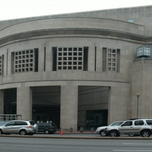 Concrete building entrance photographed from across the street. Cars in foreground.