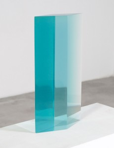 Tall light blue glass column sculpture with a diamond shaped profile. Placed on a white plinth