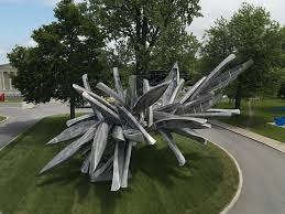 Large spiked sculpture sitting on a grass circle surrounded by a walking path