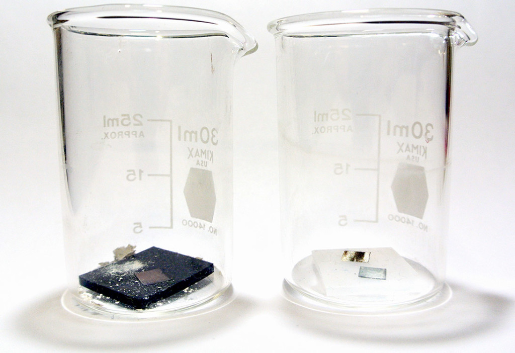 Two glass beakers. Each has small metal coupons placed in contact with exhibit material to be tested.
