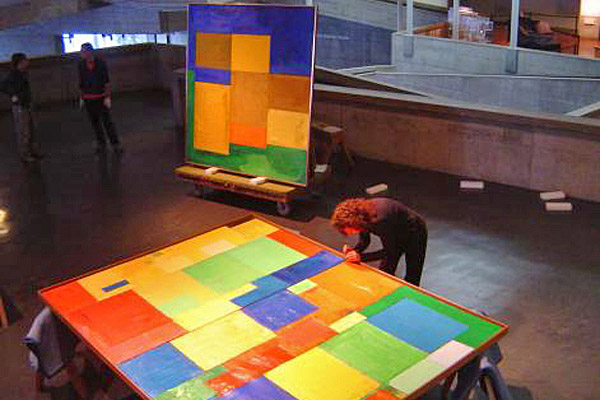 The speaker examining an oversize multi-color painting laid horizontally
