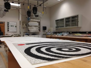 A large black, white, and orange flat artwork lays on a worktable with conservation lab benches in the background