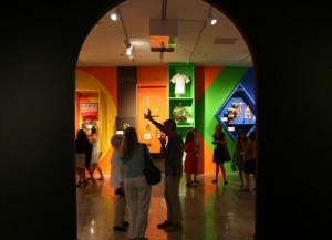 Dark archway opening into a colorful low-lit gallery with a variety of spotlights showing exhibits.