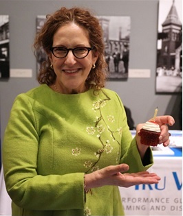 Woman in a green top holds a cupcake and smiles at the camera
