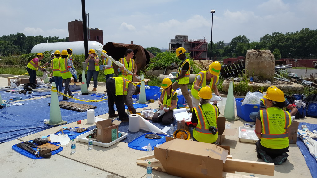 A group of people in hardhats and bright colored safety vests work to salvage practice artifacts on top of large blue tarps