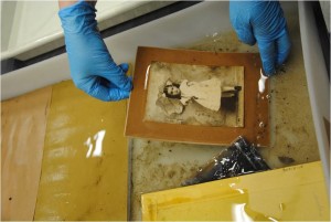 A person wearing gloves holds a wet matted black and white photograph