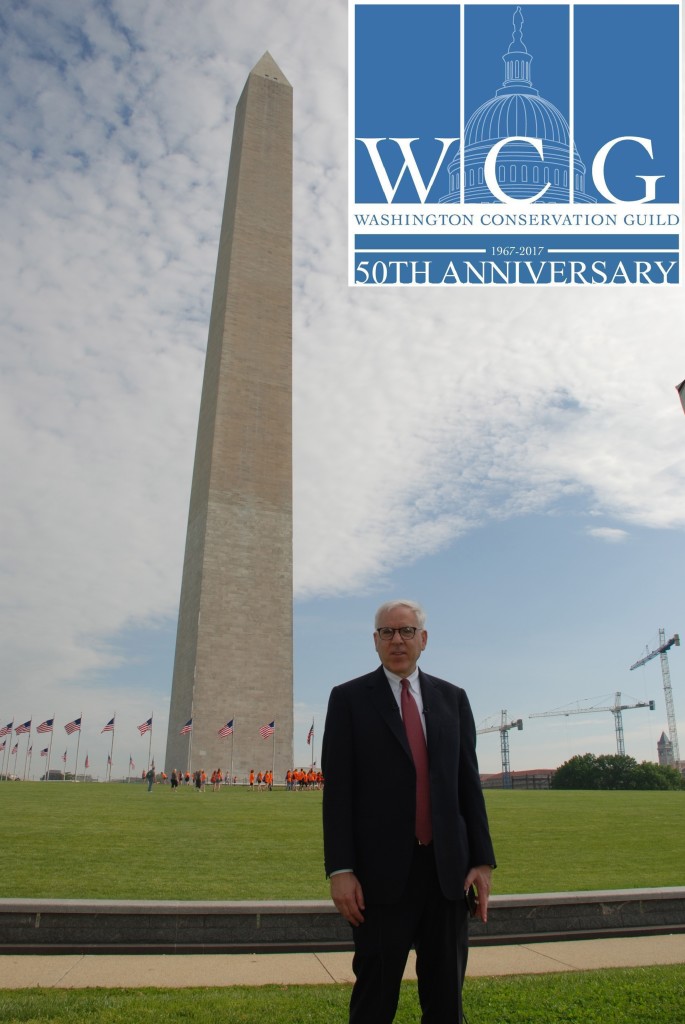 A person in a suit stands in front of the Washington Monument. The WCG logo in the corner of the image.