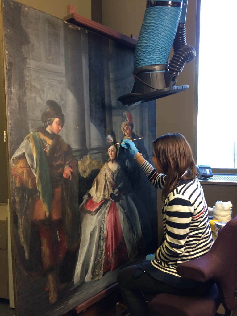 Conservator sits in front of a large painting wearing gloves and holding a cotton swab