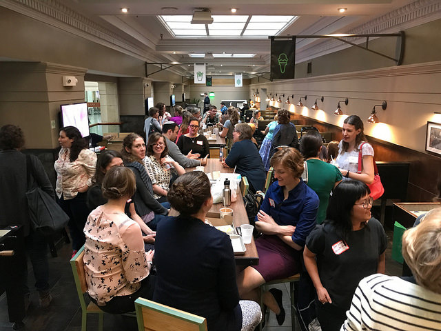 A large group of conservators sit and stand around long tables in booths