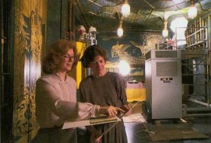 Two conservators in discussion stand in a construction site with tapestries on the walls