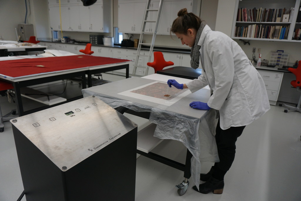Conservator holds an eyedropper over an artwork on top of a suction table