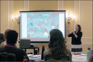 Speaker at front of lecture with a portable presentation screen.