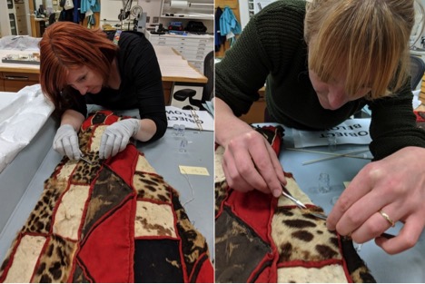 Image of the speakers working on the costume. Patchwork quilt comprised of red fabric, and variously patterned animal skins with fur, including leopard.
