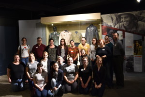 Twenty people with name tags pose in front of a display case in the musuem