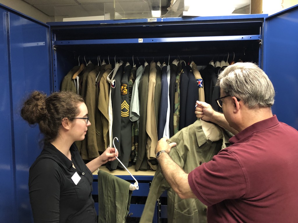Two volunteers hold hangers with olive green uniform jacket and slacks