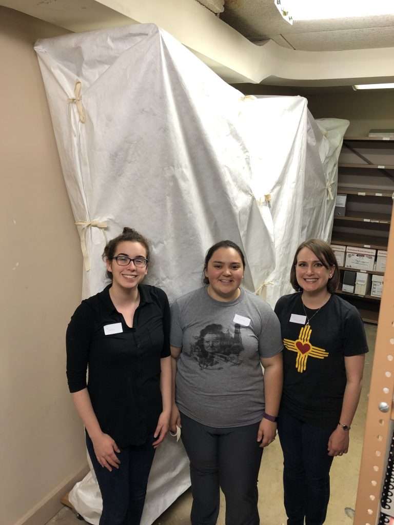Three volunteers standing in front of a large white cover in collections storage