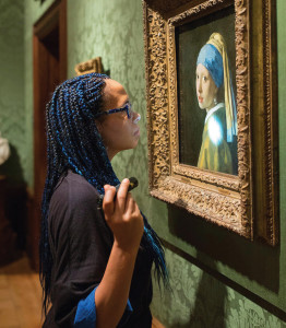 A conservator examines the Vermeer classic painting Girl with a Pearl Earring with a flashlight in the gallery.
