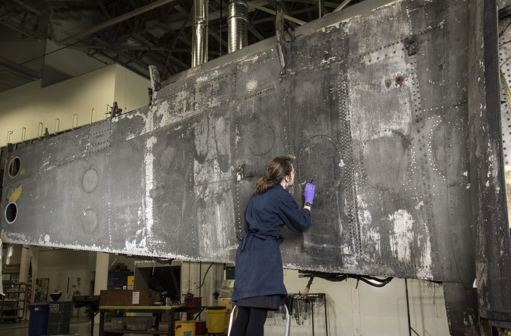 Conservator inpainting damaged vertical aircraft surface.