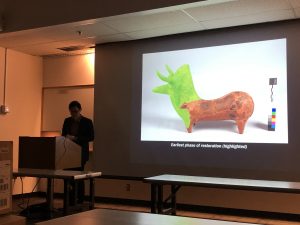 Speaker at front of lecture hall with presentation projected behind. Head and neck of figurine highlighted in green.