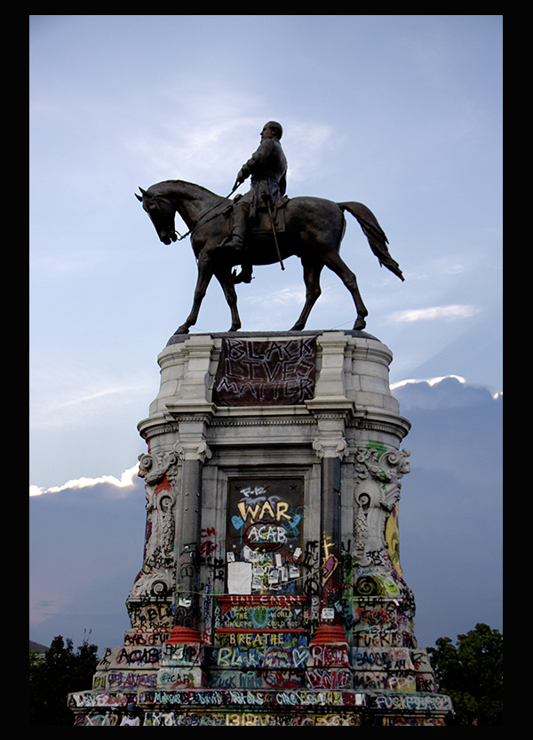 Confederate monument with graffiti covering base and Black Lives Matter banner.