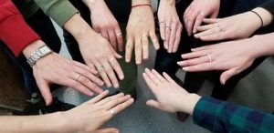 A circle of ten people put their hands with silver ring into the middle