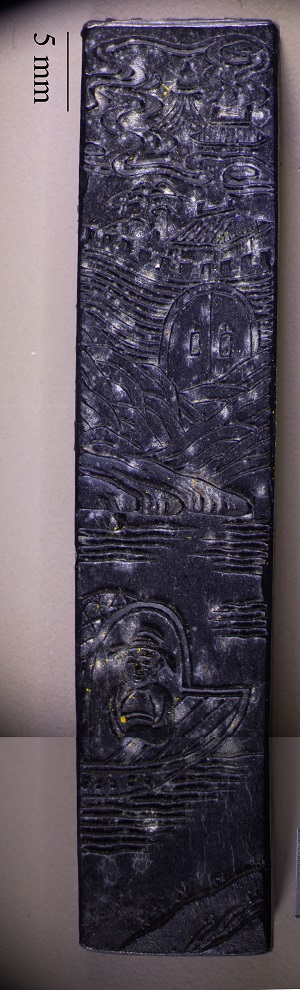 Incised black ink stick depicting figure in foreground and mountains and structures in background