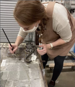 A conservator holding a paint brush working to remove facing material with small corner of cleaned panel