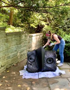 A professional conserving a dark-colored outdoor stone sculpture wearing personal protective equipment and working outside.