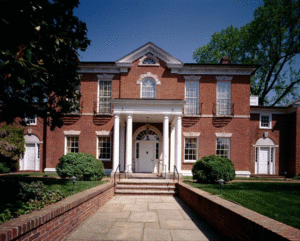 Brick stately home with white columns. Stone sidewalk and steps surrounded by a brick wall and evergreen bushes