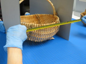 Gloved hands hold up a tape measure to a natural fiber woven basket