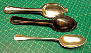 Gray metal spoon in a spoon mold, an empty spoon mold, and a gray metal spoon lined up on a worktable