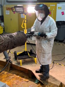 A conservator in full personal protective equipment holes a drill at the end of a cannon undergoing treatment.
