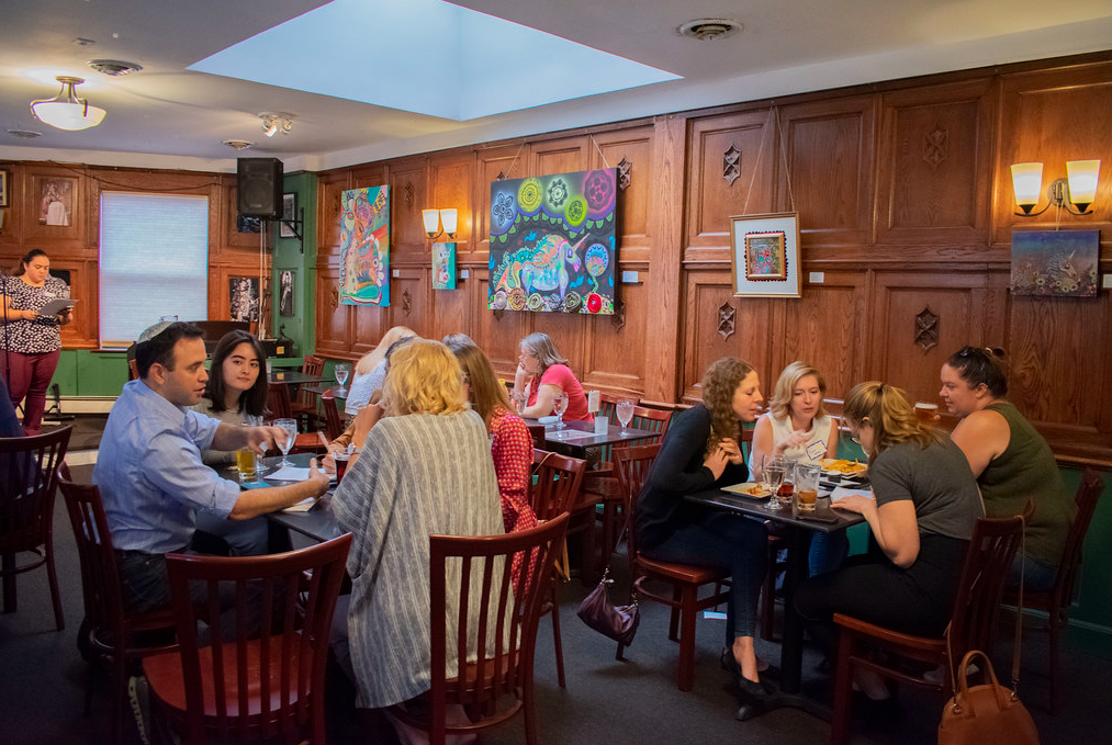 Members gathered in small trivia teams seated tables in a restaurant. 