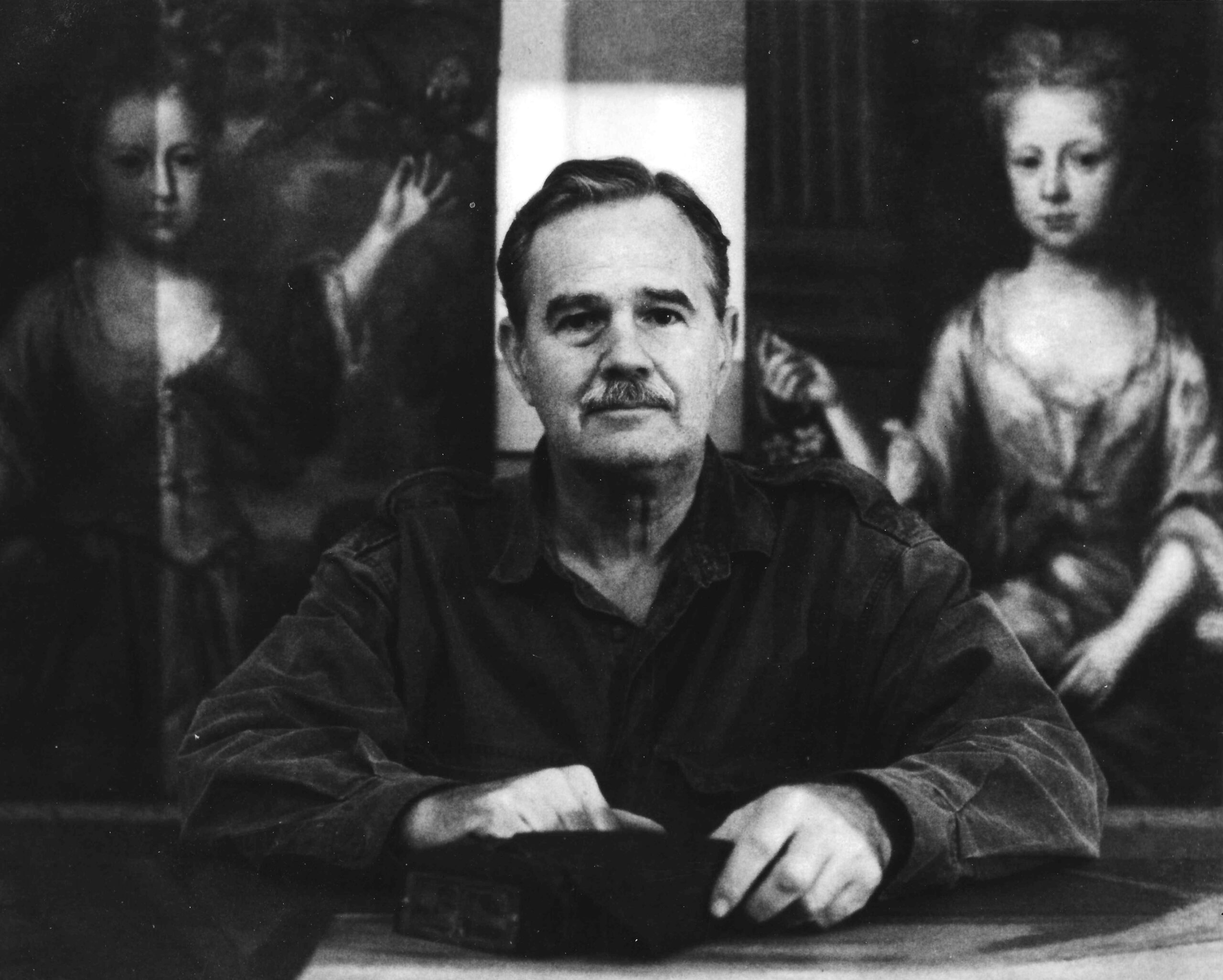 Black-and-white photograph of a conservator sitting at a table in front of two partially cleaned paintings.