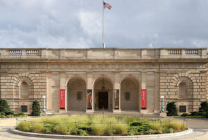Freer gallery courtyard with fountain framed with greenery in the foreground and white-stone sub-style Mannerist building topped with a flag.