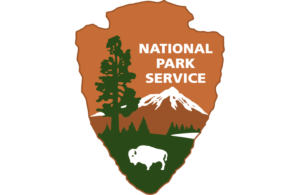 National Parks Service logo, consisting of a brown arrowhead shape with an inset mountanous landscape with while buffalo figure and agency name overlaid.