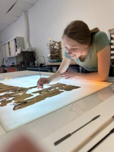 A smiling professional leans over a lightbox where she assembles torn fragments of paper.
