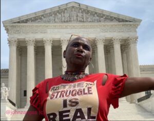 A woman stands outside the US supreme court wearing a red tshirt with the words "1921 - 2021, The Struggle is Real"