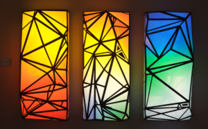 Three colorful glowing recntables with a color gradent from yellow to red on the left, Blue to green to white on the right, and all previously mentioned colors in the middle rectangle. Dark angular, prismatic lines super imposed over the color fields.