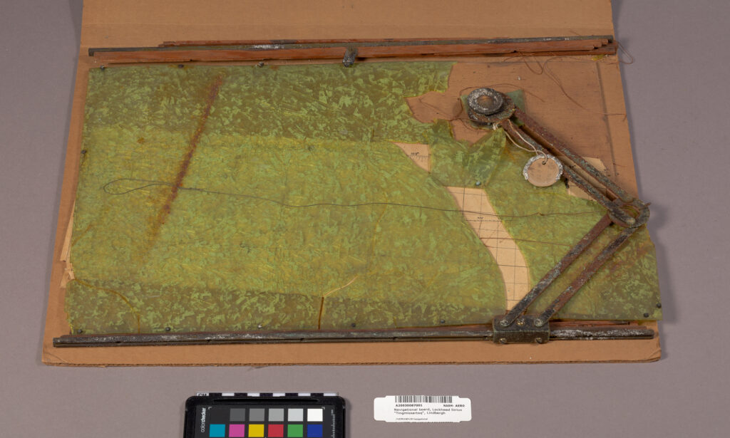 A navigational board from the LIndbergh's Lockheed Sirius "Tingmissartoq", consisting of a green plastic over a board with a steel drafting arm.