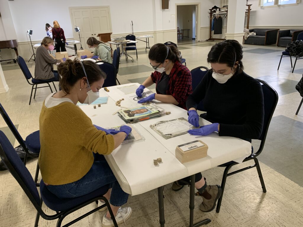 Volunteers around a table working to surface clean triage objects with small segments of soot sponge