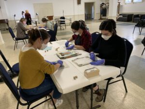 Volunteers around a table working to surface clean triage objects with small segments of soot sponge