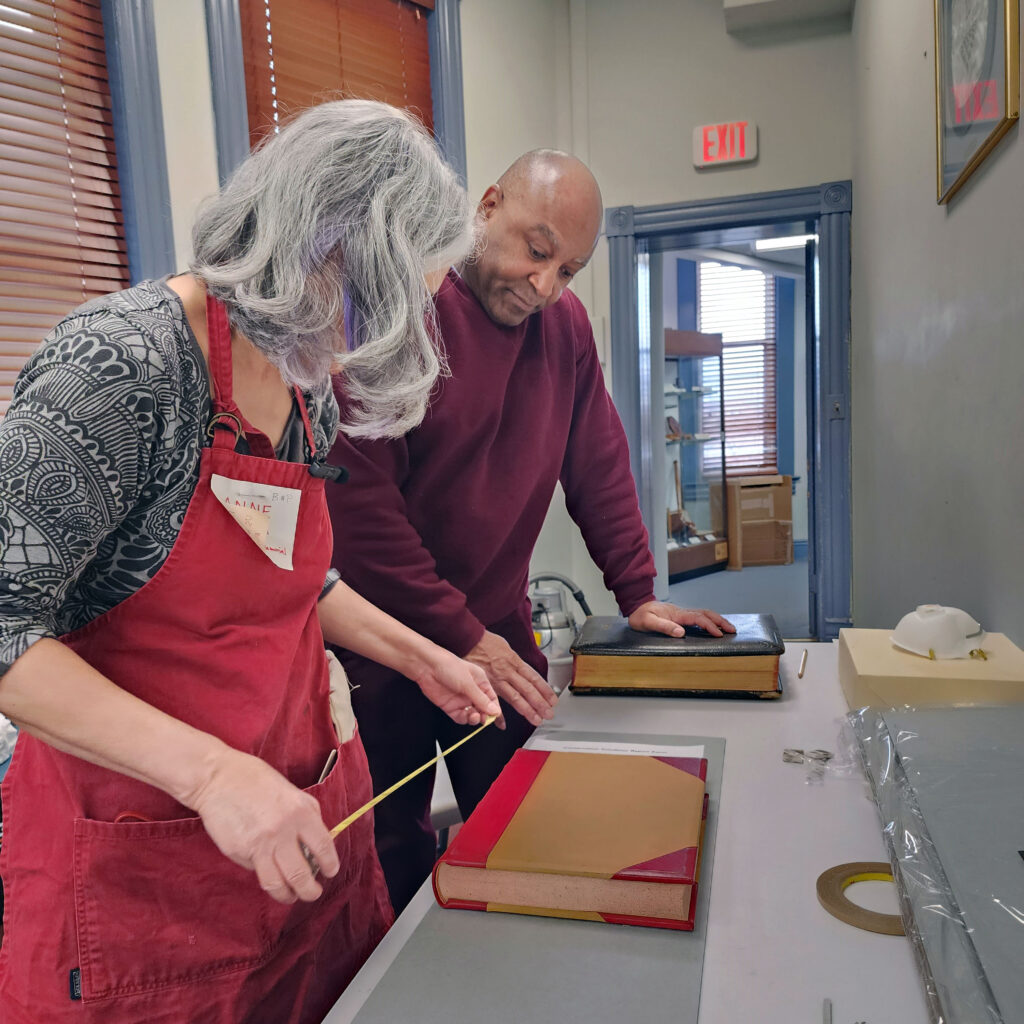 A woman measures a book, and a second person observes.