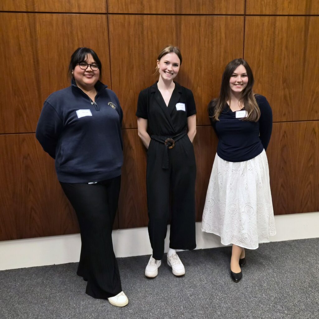 Three people standing in a row and smiling.
